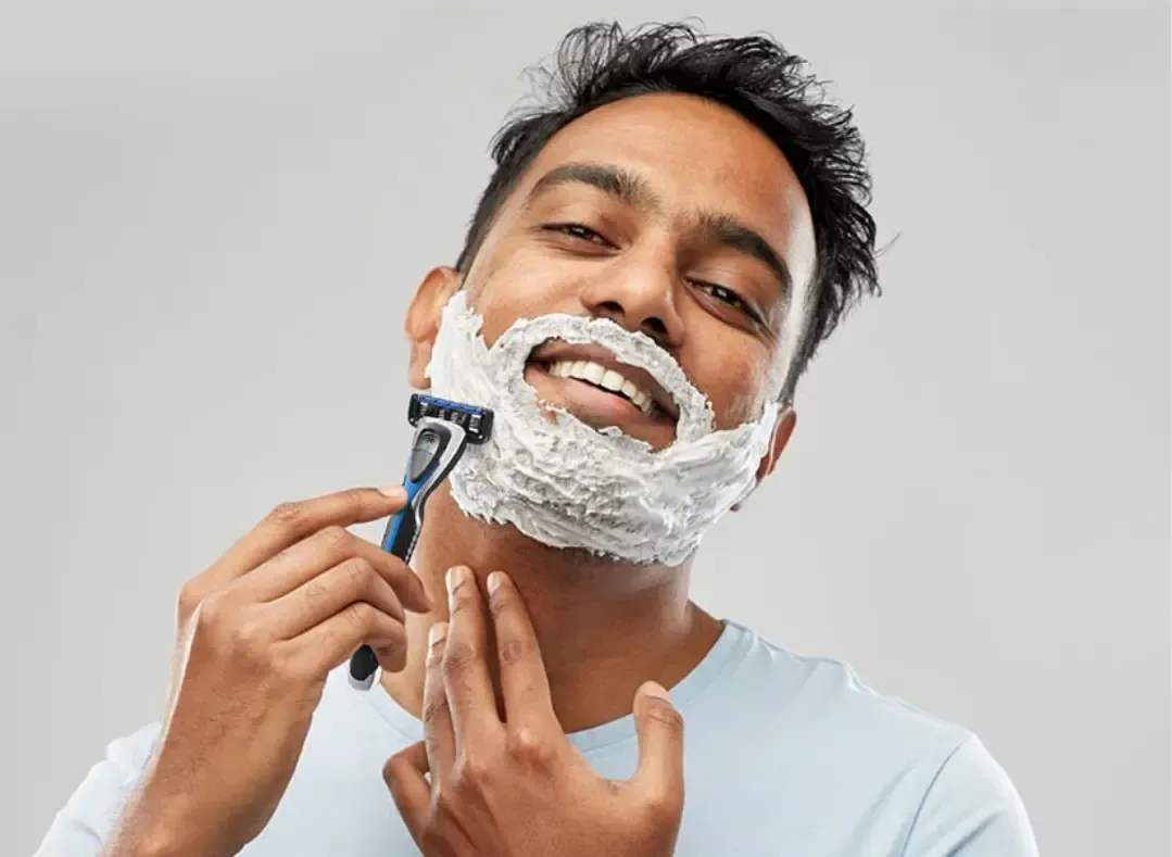 A smiling man shaving with a razor and shaving cream