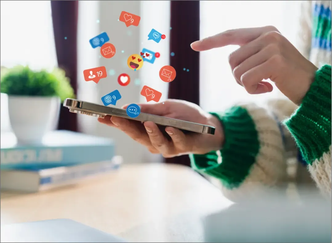 A person holding a smartphone with floating social media icons representing likes, shares