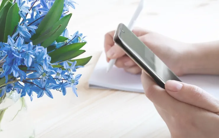 A person holding a smartphone while writing notes