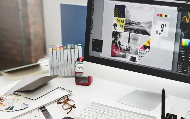 A creative workspace featuring a desktop computer displaying a graphic design project