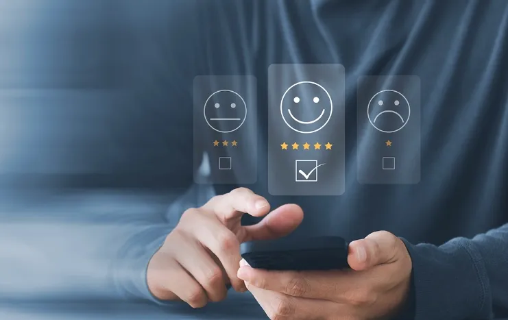 A person using a smartphone with smiley face icons representing a customer feedback system