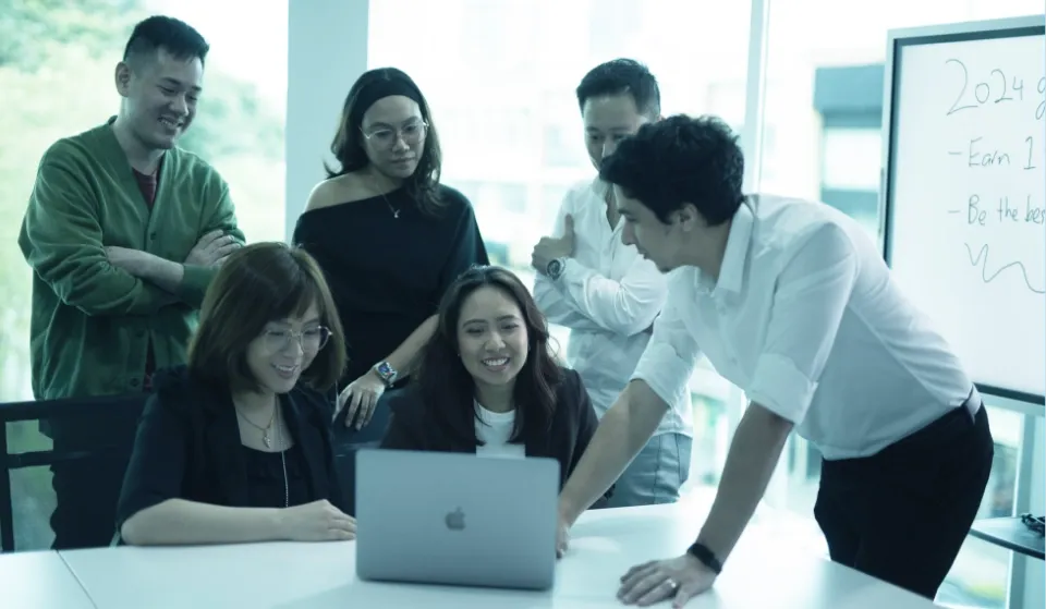 Trinergy team collaborating around a laptop, focusing on a project with a positive and productive approach.