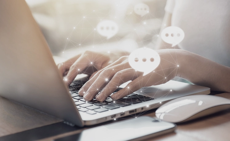 Hands typing on a laptop with digital chat icons, symbolizing Trinergy's advanced communication and digital collaboration solutions.