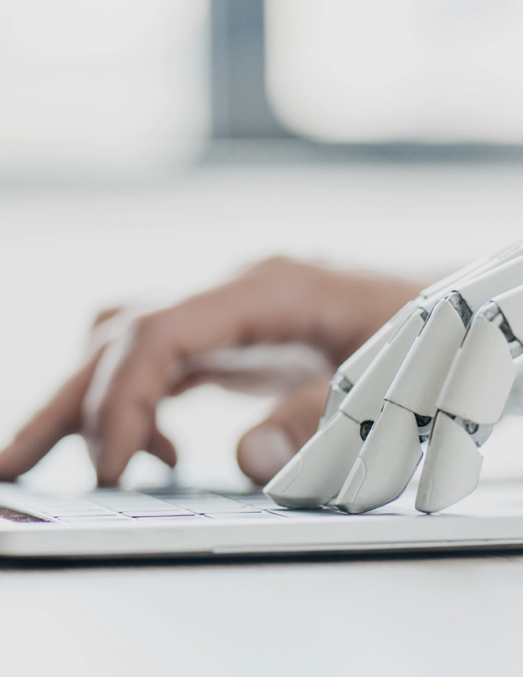 Human hand working alongside a robotic hand on a laptop, symbolizing Trinergy's focus on AI and human collaboration for digital solutions.