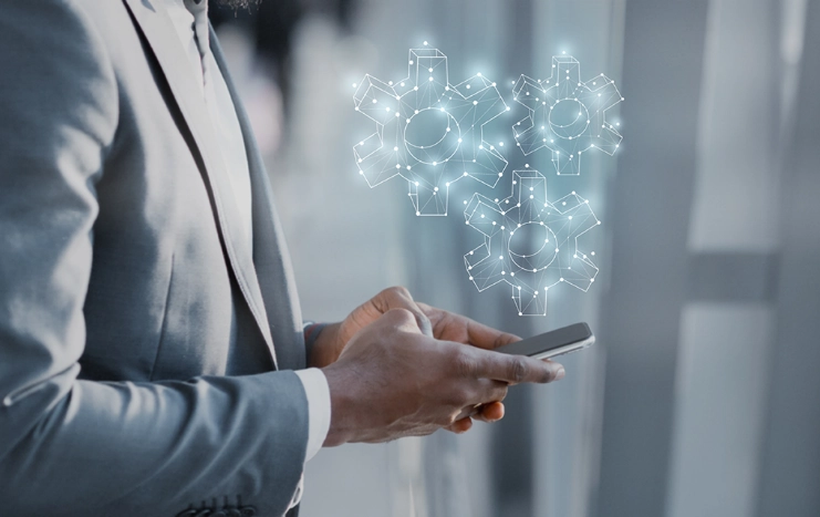 Business professional using a smartphone with virtual gear icons, symbolizing Trinergy's automation and technology integration solutions.